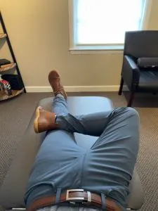 A patient's leg positioned for the FABER test, ankle crossed above the opposite knee, on a treatment table at REACH Rehab + Chiropractic