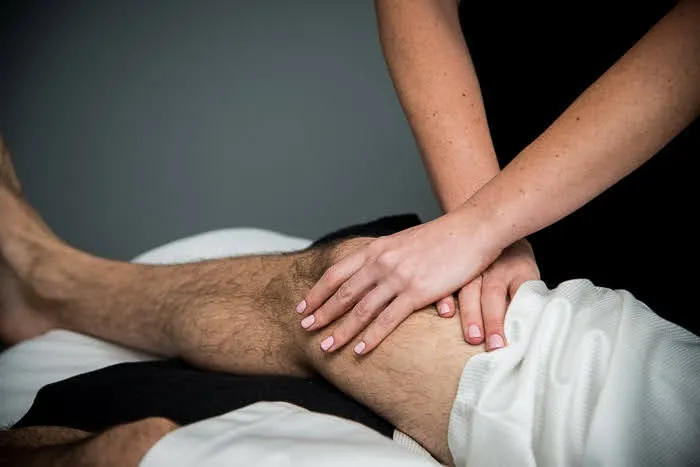 A practitioner’s hands performing manual bodywork on a patient’s knee