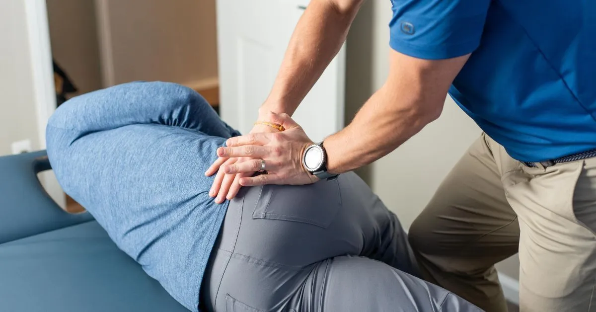 A REACH clinician pressing both hands into a specific point on a patient's hip and glute to locate the source of the pain